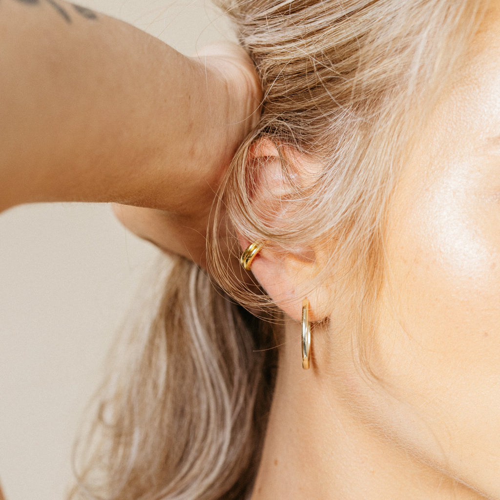Close-up of a person with blonde hair wearing gold hoop earrings and the elegant Cleo Cuffs cartilage earring, hand tucked behind ear.