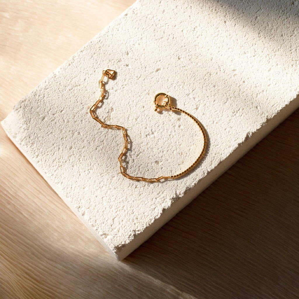 The Klara Tennis Bracelet is displayed on a textured white stone surface with soft natural light and shadows, ideal for lovers of minimalist jewelry.