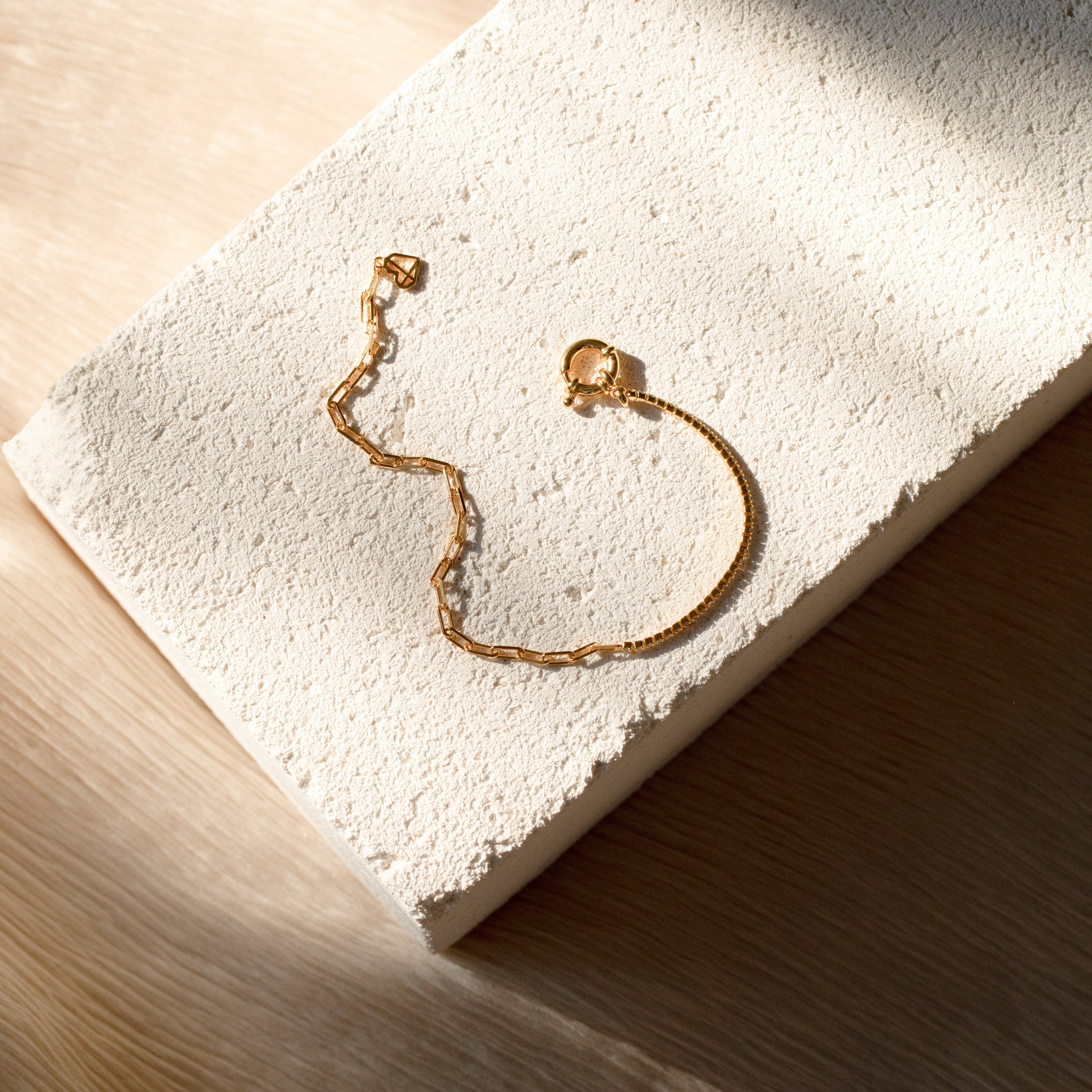 The Klara Tennis Bracelet is displayed on a textured white stone surface with soft natural light and shadows, ideal for lovers of minimalist jewelry.