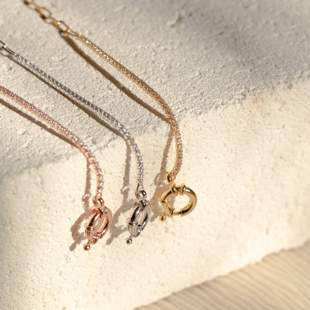 The Klara Tennis Bracelet—a sleek, minimalist piece in rose gold, silver, or gold—makes a perfect addition to any jewelry collection and is displayed on a textured, light-colored surface.