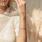 A woman in a white textured top wears the Rope Chain Bracelet, featuring a twisted gold design, as sunlight casts patterns on her skin.