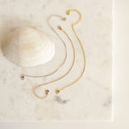 The polished Box Chain Bracelet in gold and silver rests beside a seashell on a marble surface, paired with two delicate chain bracelets.