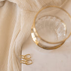 The Amanda Link Earrings in 18K Gold are displayed on a white marble surface with a cream-colored fabric background.