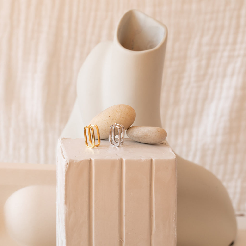 The Nina Link Earrings in Rose Gold, displayed on stones with abstract ceramic shapes, evoke the modern appeal of geometric hoop earrings.