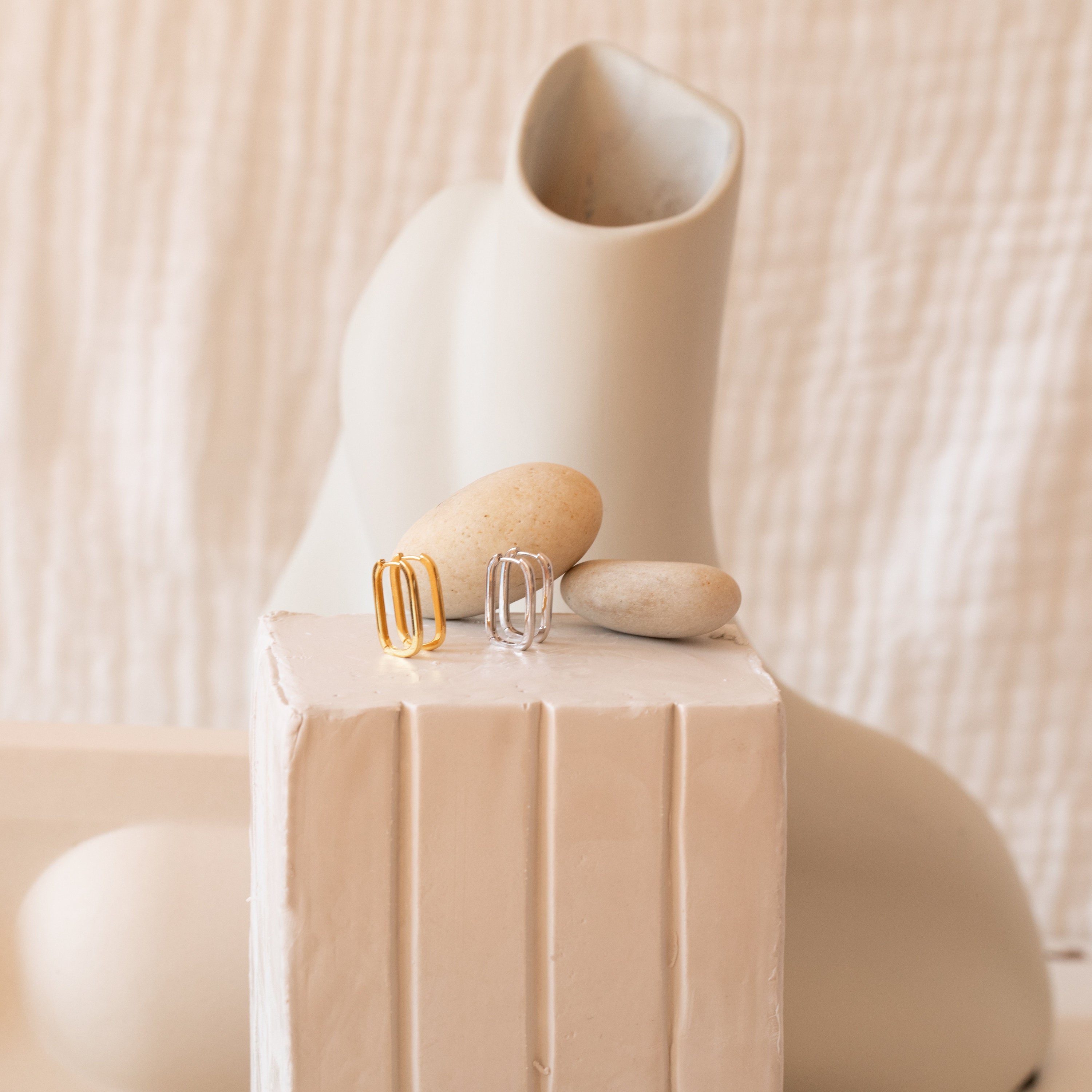 The Nina Link Earrings in Rose Gold, displayed on stones with abstract ceramic shapes, evoke the modern appeal of geometric hoop earrings.