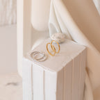 Two pairs of rings—one gold, one silver—are displayed on a white textured pedestal with a small stone, making them perfect accents for the city girl who loves the elegant style of Classic Hoops in Sterling Silver.