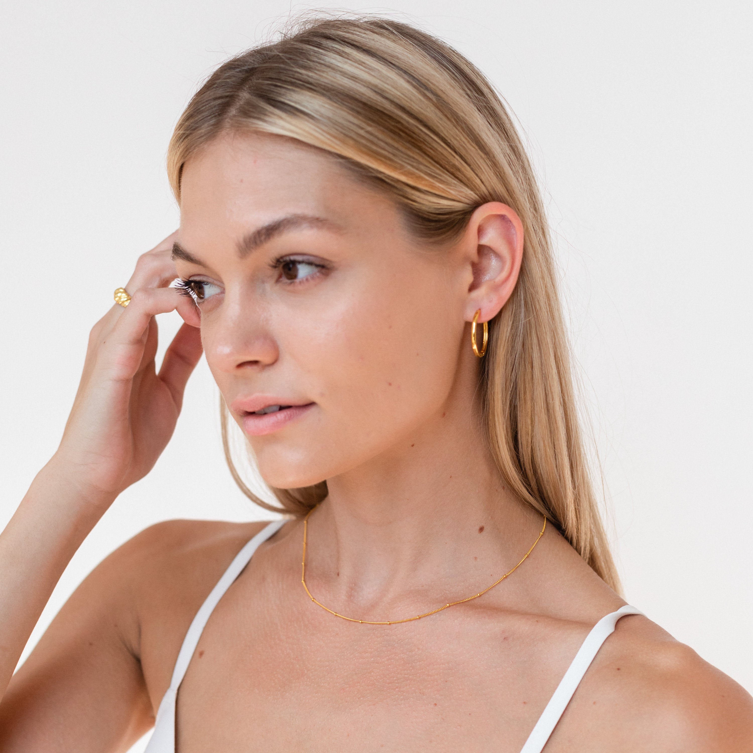 A city girl wearing Classic Hoops softly touches her eye.