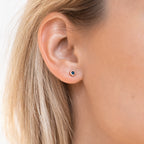 Close-up of a woman's ear with straight blonde hair, wearing Noir Diamond Studs—unique small round earrings featuring a dark center.