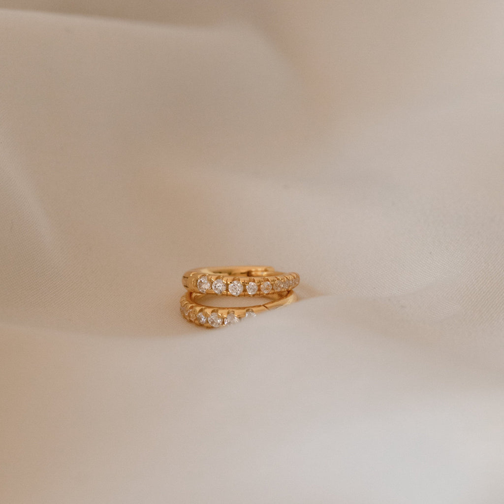 The Vera Pave Huggies are displayed on a soft beige fabric background, ideal for pairing with minimalist earrings or other everyday jewelry.