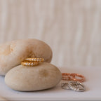 The Vera Pave Huggies in Rose Gold, displayed on smooth beige stones with minimalist rings and earrings, create a refined everyday jewelry collection against a soft background.