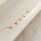 Personalized jewelry shines with this Pave Letter Necklace in Rose Gold, featuring letter charms spelling GRAT on a white ceramic dish.