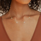 Gold necklace featuring four spaced pave letter charms spelling “MAMA”, set on a delicate chain and styled just above the collarbone. Worn with a rust-toned tank top.