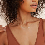 A woman wears the Pave Mama Letter Necklace—an elegant motherhood jewelry piece—paired with a rust tank top, shown from shoulders to chin.