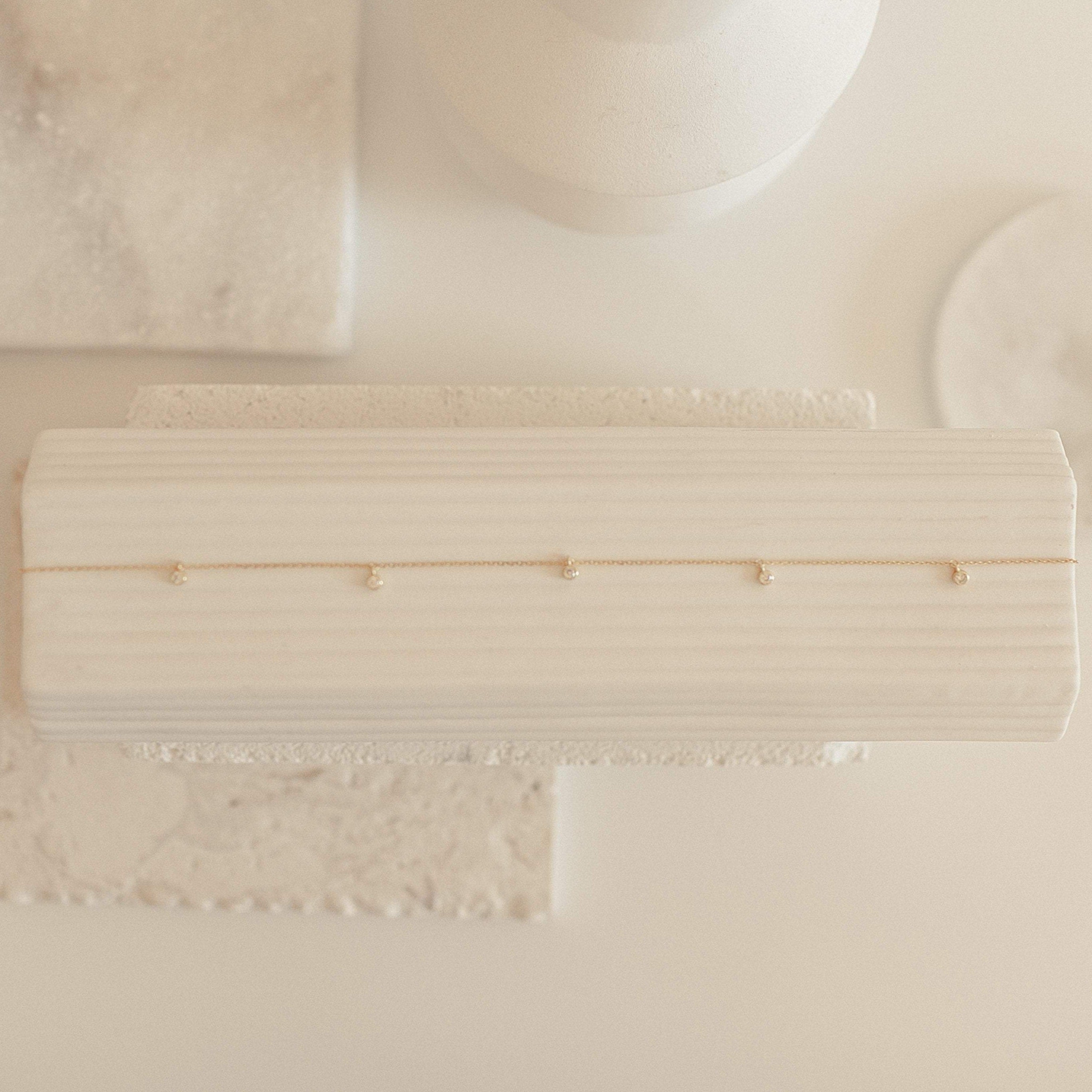 The Diamond Station Necklace features delicate gold with sparkling gems, displayed on a textured white surface in soft lighting—modern elegance for a timeless accessory.