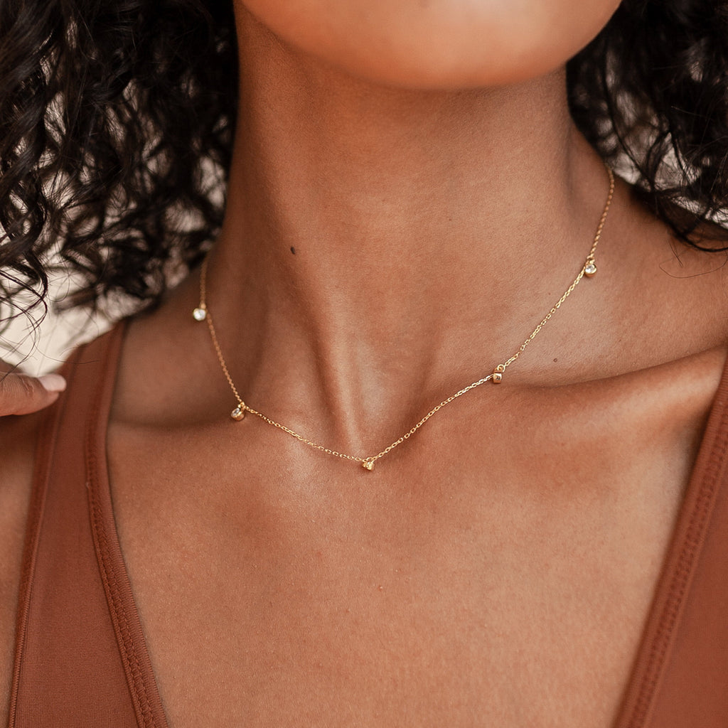 Close-up of a woman in a brown top wearing the Diamond Station Necklace, featuring delicate gold beads that highlight its modern elegance.