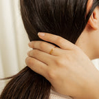 A hand wearing the Petite Tiny Name Ring gently holds the back of a woman's head, gathering her long dark hair.