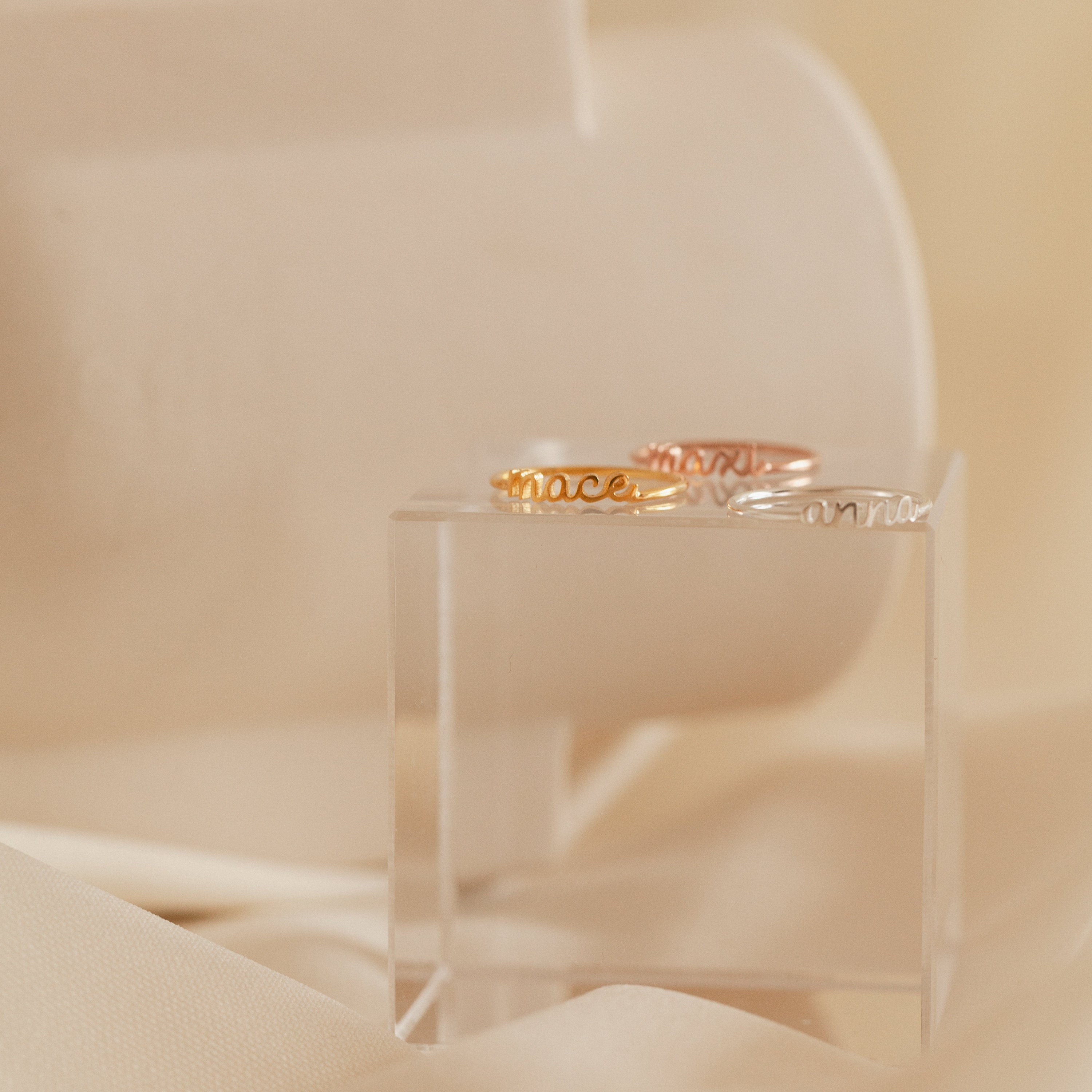 A pair of Petite Tiny Name Rings displayed on a clear box.