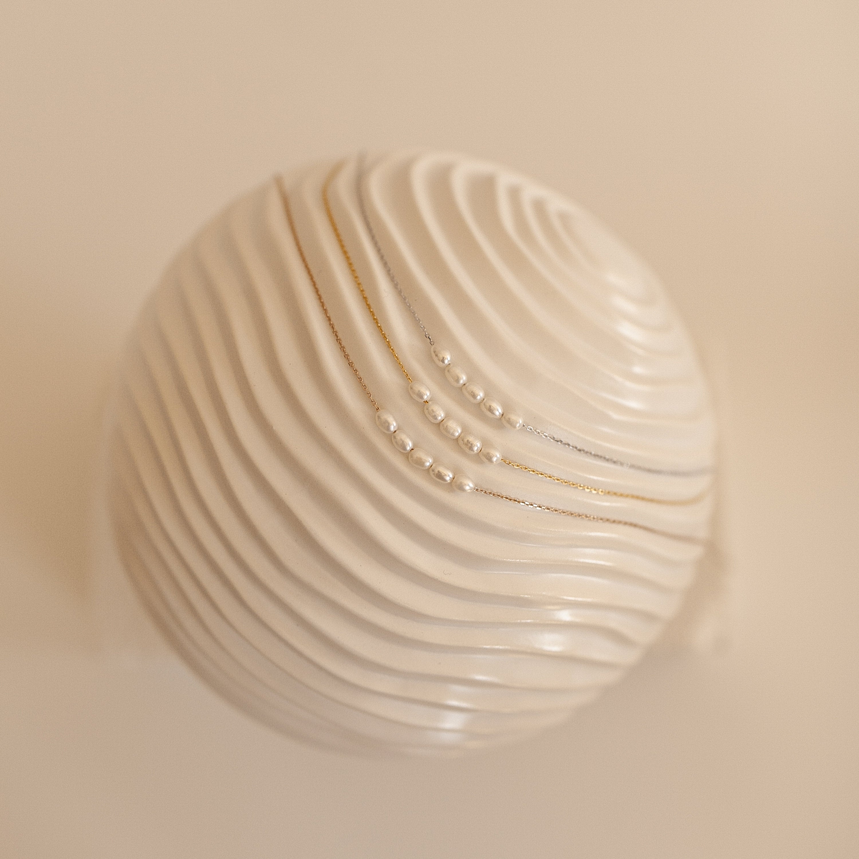 A close up of Pearl Beaded Necklaces in silver, gold, and rose gold on a sculptural wavy surface.