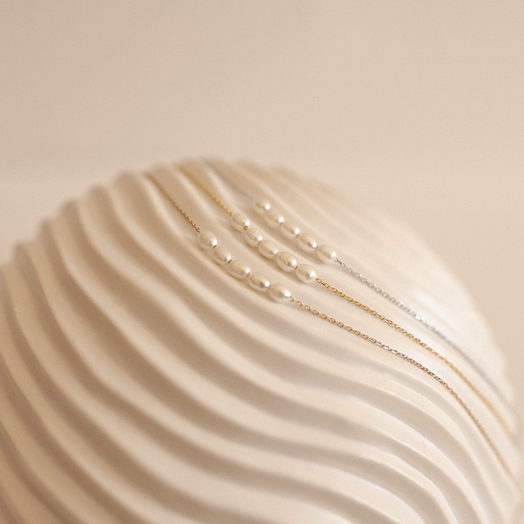 Gold,Silver, and Rose Gold Pearl Bead Necklaces displayed on a textured, wavy white ceramic surface. 