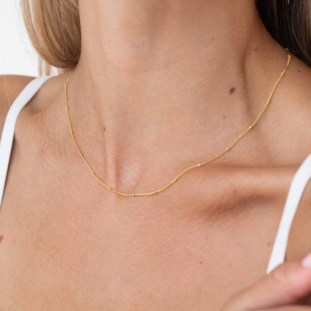 Close-up of a gold Satellite Necklace around a woman’s neck, worn with a white tank top.