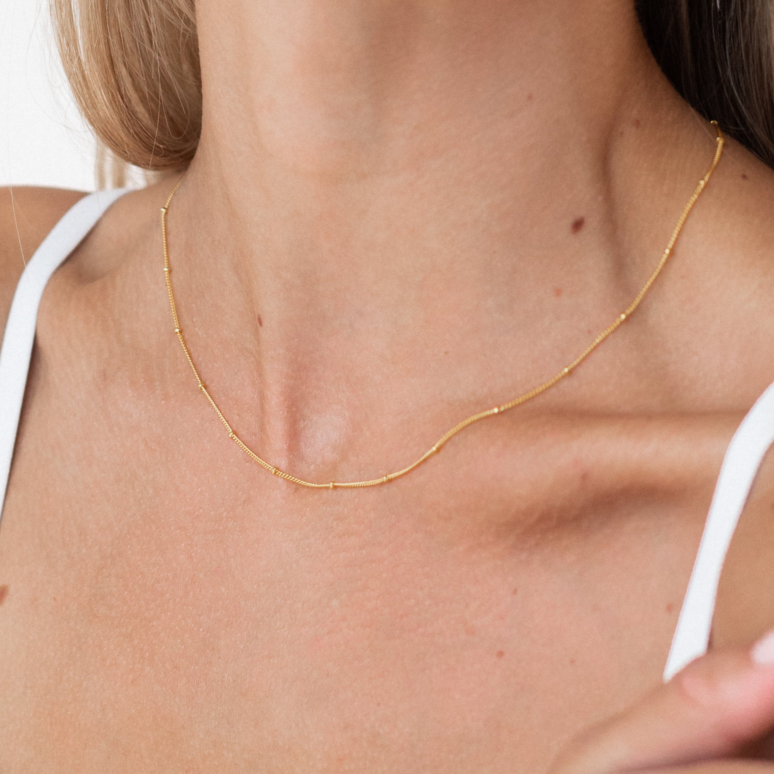 Close-up of a gold Satellite Necklace around a woman’s neck, worn with a white tank top.