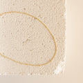 A gold Satellite Necklace arranged in an oval shape atop a textured, off-white stone surface.
