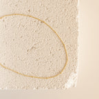 A gold Satellite Necklace arranged in an oval shape atop a textured, off-white stone surface.