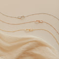 The Linked Pendant Necklace in Rose Gold is featured, displayed on soft, cream-colored fabric.