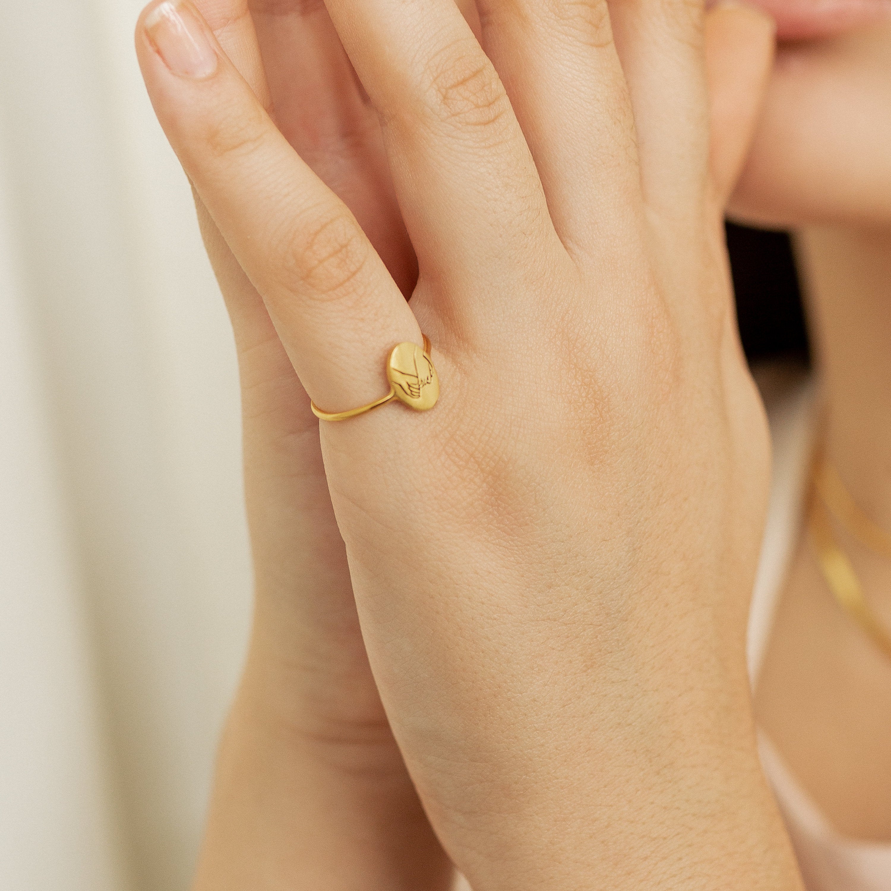 A person wears the Gestures of Love Ring, a thin gold band engraved with a face design that captures subtle symbolic hand gestures in figurative jewelry.