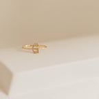 The Pave Initial Ring, featuring a diamond-encrusted gold letter G, rests on a white surface with a beige background.