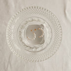 The Pearl Hoops feature white pearls and rest on a textured clear glass plate, making these earrings an elegant accessory for everyday wear.