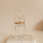 The Baroque Pearl Necklace is elegantly draped over a clear glass of water on a white surface, showcasing its unique pendant.