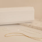 A soft-focus image of gold and silver Singapore Twist necklaces arranged flatly on a neutral-toned surface.