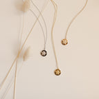 The Bee Coin Necklace set features two pendants—one silver, one gold—displayed on a beige background with dried grass for a chic, layered honeybee jewelry look.