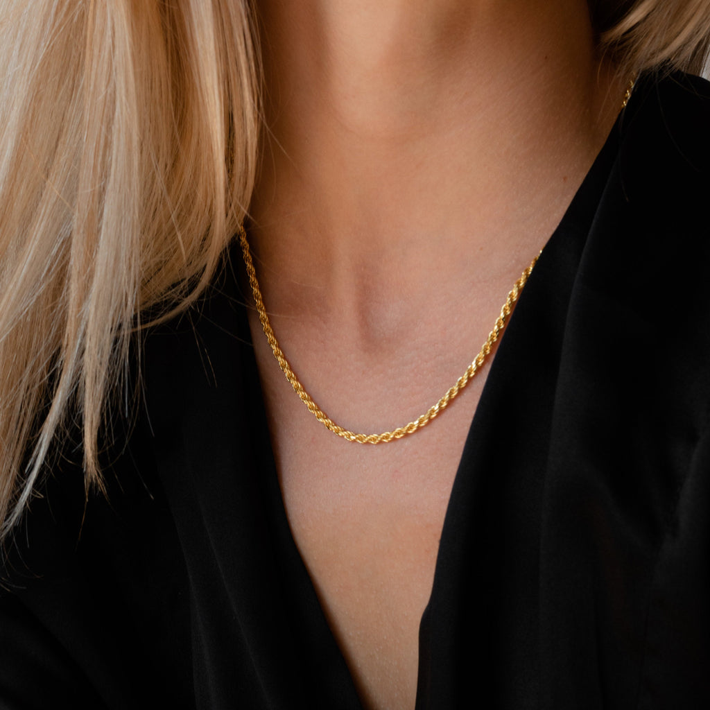 Gold rope chain necklace worn by a model in a black blouse.