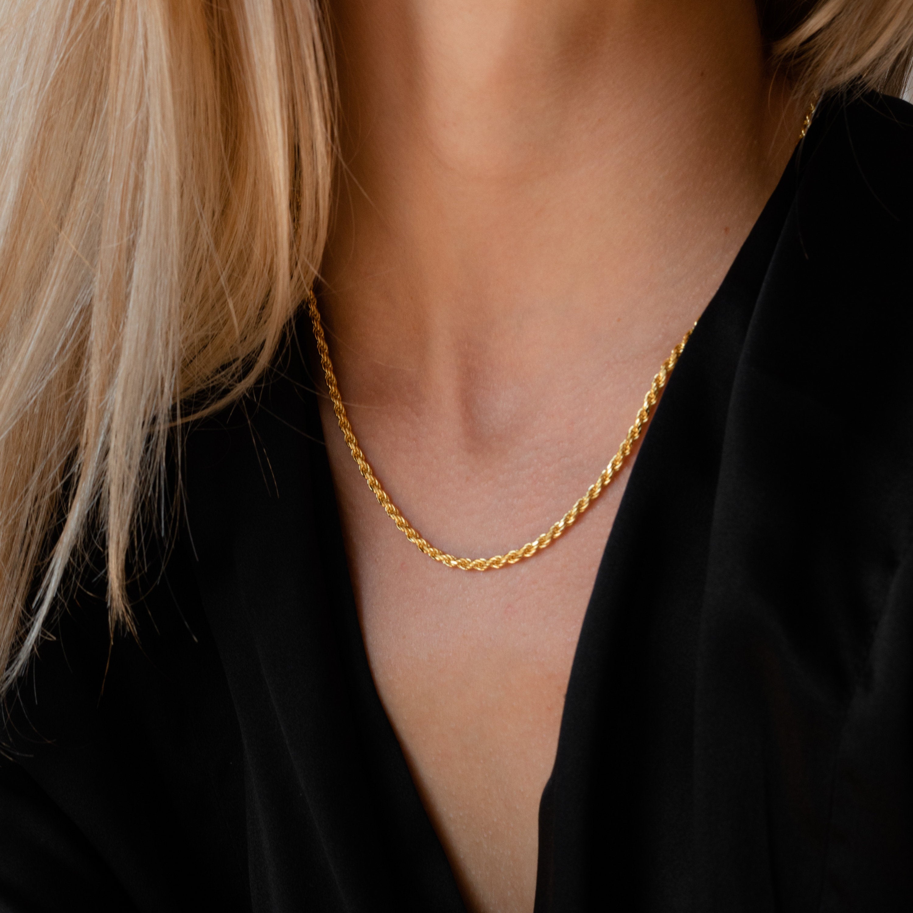 Gold rope chain necklace worn by a model in a black blouse.