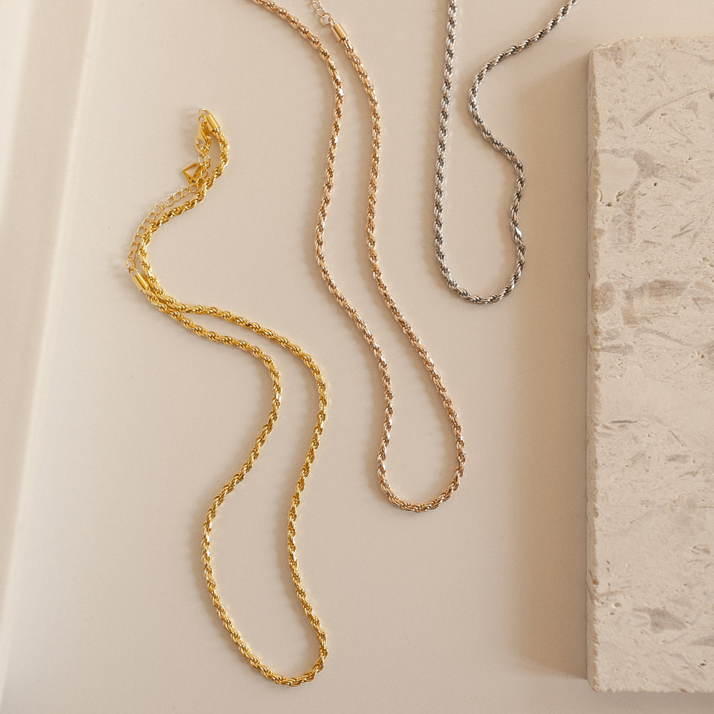 Gold, rose gold, and silver rope chain necklaces laid out side by side on a light surface.