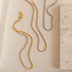 Gold, rose gold, and silver rope chain necklaces laid out side by side on a light surface.