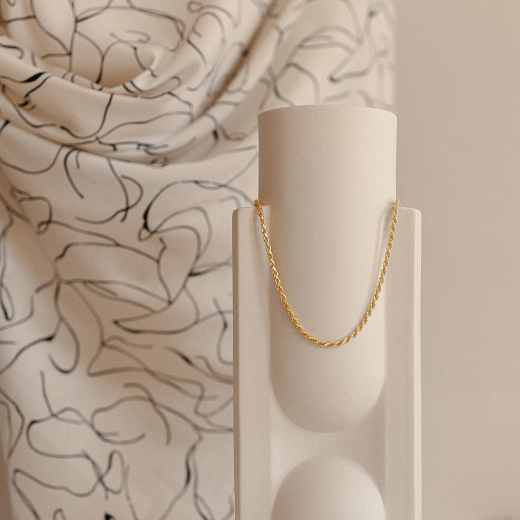 Gold rope chain necklace displayed neatly against a cylindrical ceramic stand.