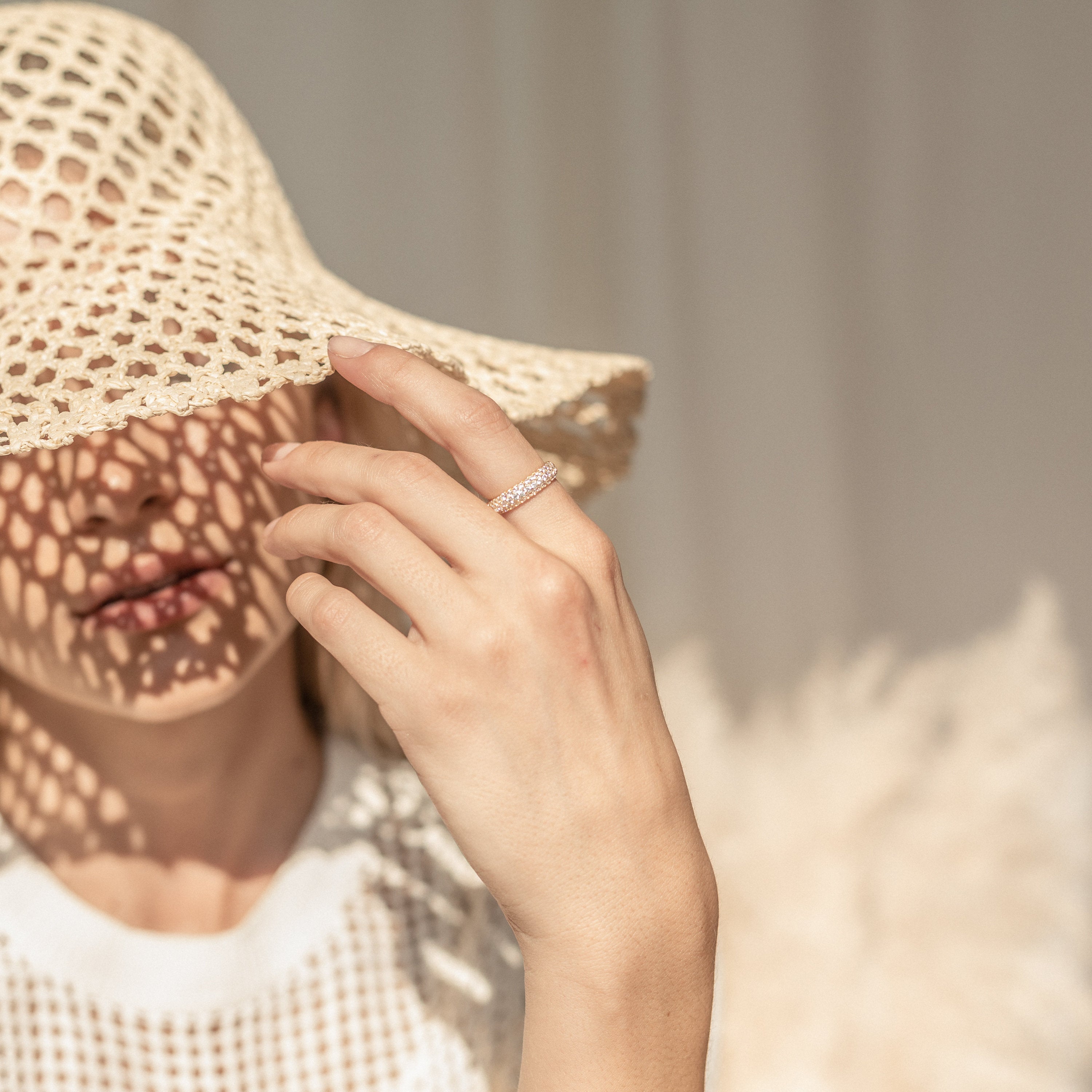 Woman in a sunhat with shadow patterns on her face, wearing a white top and highlighting the Pave Dome Ring alongside her diamond ring.