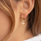 Close-up of a woman's ear wearing Starburst Huggies—gold earrings featuring a star-shaped pendant accented with pavé diamonds.