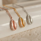 The Pave Shell Necklace, available in rose gold, gold, and silver, adds coastal cottage charm to any outfit and looks stunning when displayed on a light, textured surface.