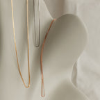 Three box chain necklaces in gold, silver, and rose gold finishes elegantly displayed across a soft cream sculpture, showcasing all available metal tones