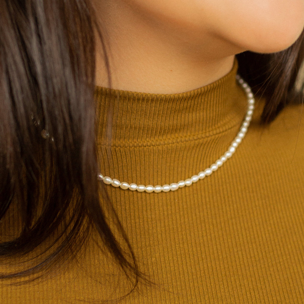 Close-up of a woman wearing the Pearl Choker Necklace paired with a mustard yellow ribbed turtleneck top.