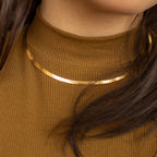 A gold herringbone necklace worn over a brown ribbed turtleneck top.