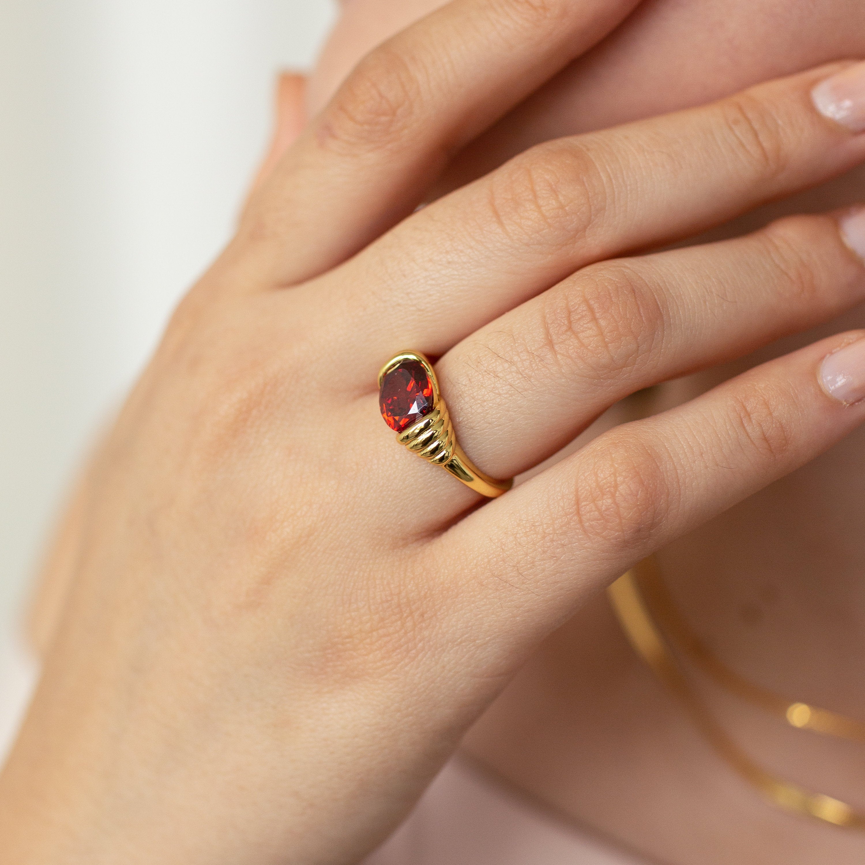 A hand adorned with the Garnet Signet Ring in gold, vintage-inspired, fingers gently touching the face.