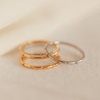The Sprinkle Diamond Ring, a delicate stackable piece in gold and silver, is displayed on a soft beige fabric background.