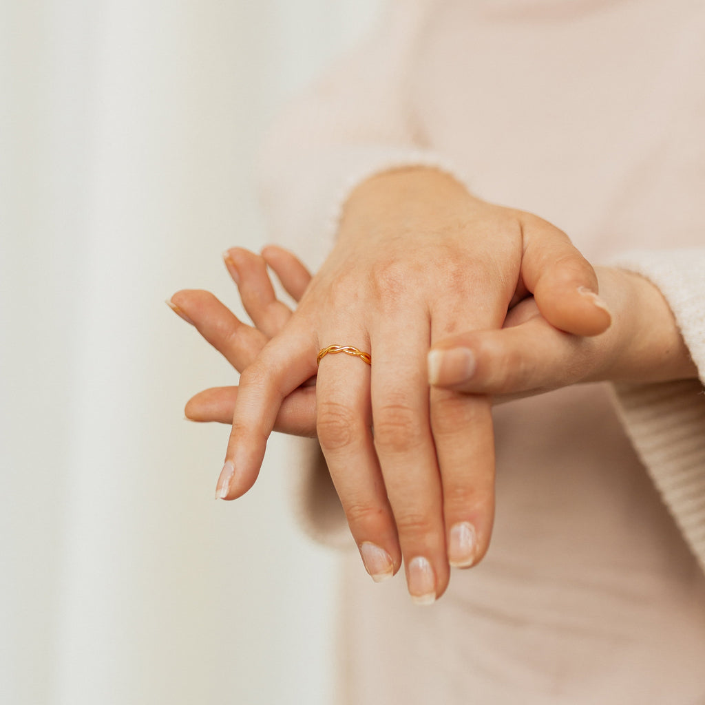A person wearing the Braided Ring on their finger gently touches their hand, set against a neutral background.