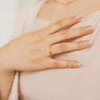 A hand wearing the Braided Ring rests on a chest, displaying neat, natural nails and a light pink top.