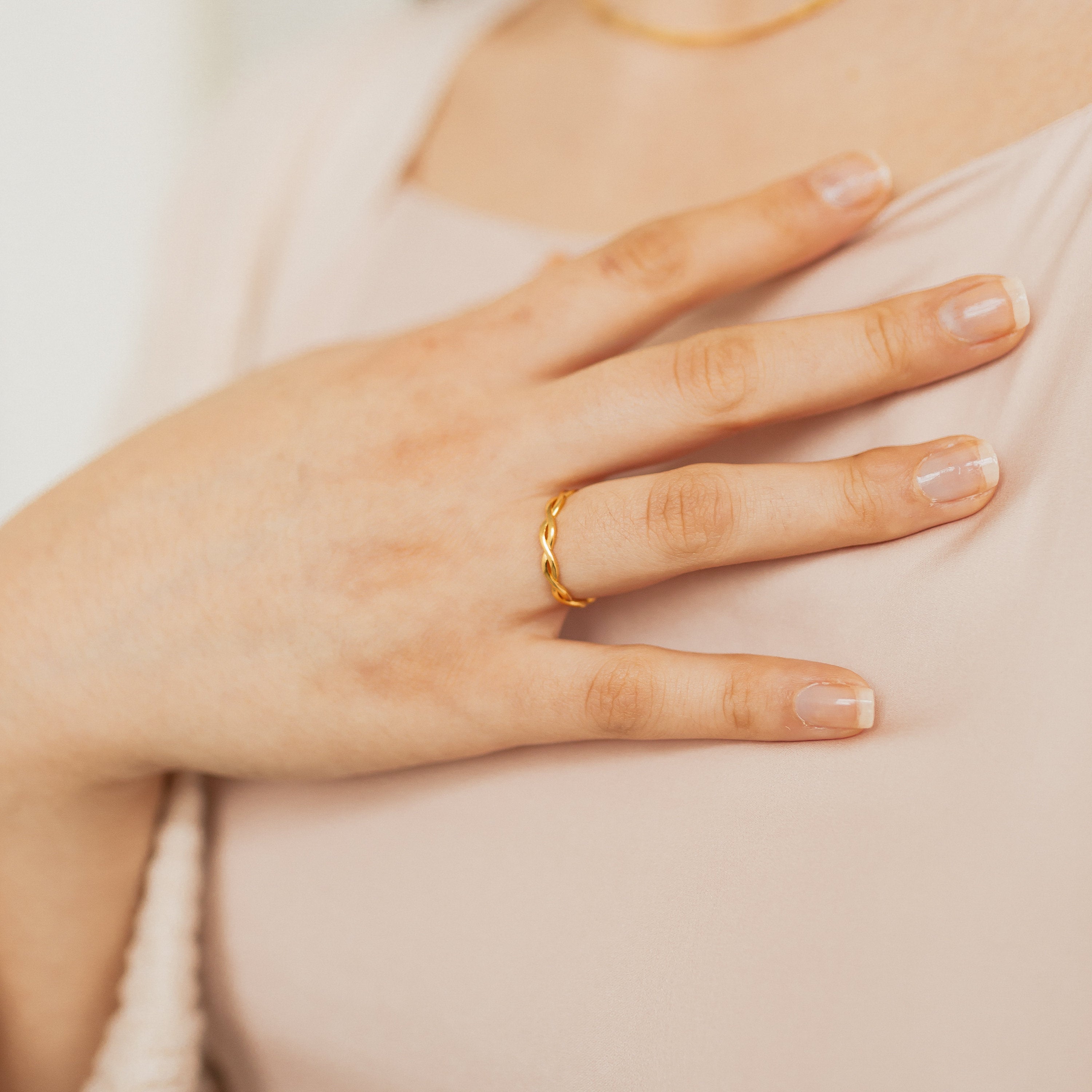 A hand wearing the Braided Ring rests on a chest, displaying neat, natural nails and a light pink top.